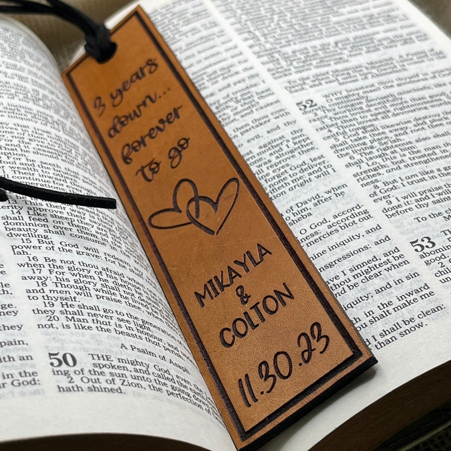 Personalized third anniversary leather bookmark with engraved names and date on an open book