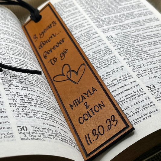 Personalized third anniversary leather bookmark with engraved names and date on an open book