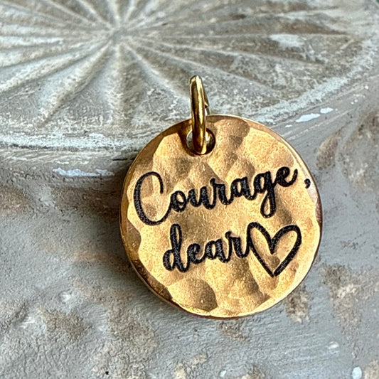 Gold pendant with 'Courage, dear heart' engraving on a textured surface
