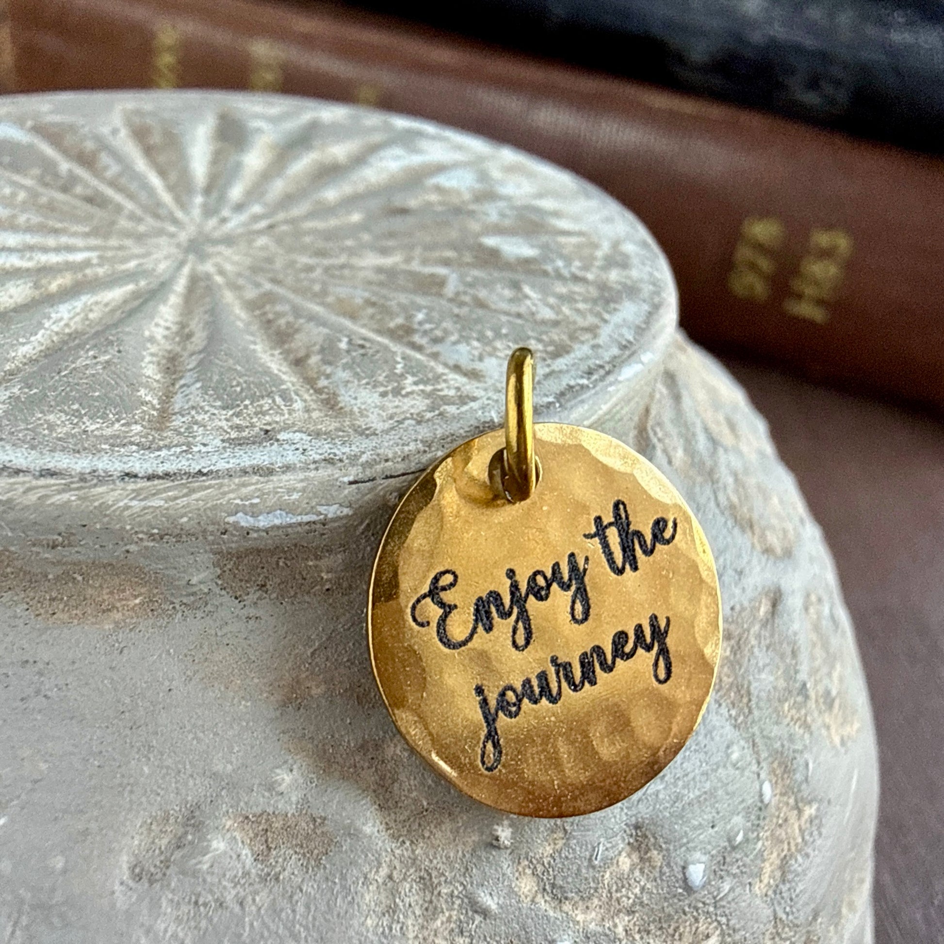 Gold pendant with 'Enjoy the journey' engraving on a stone surface
