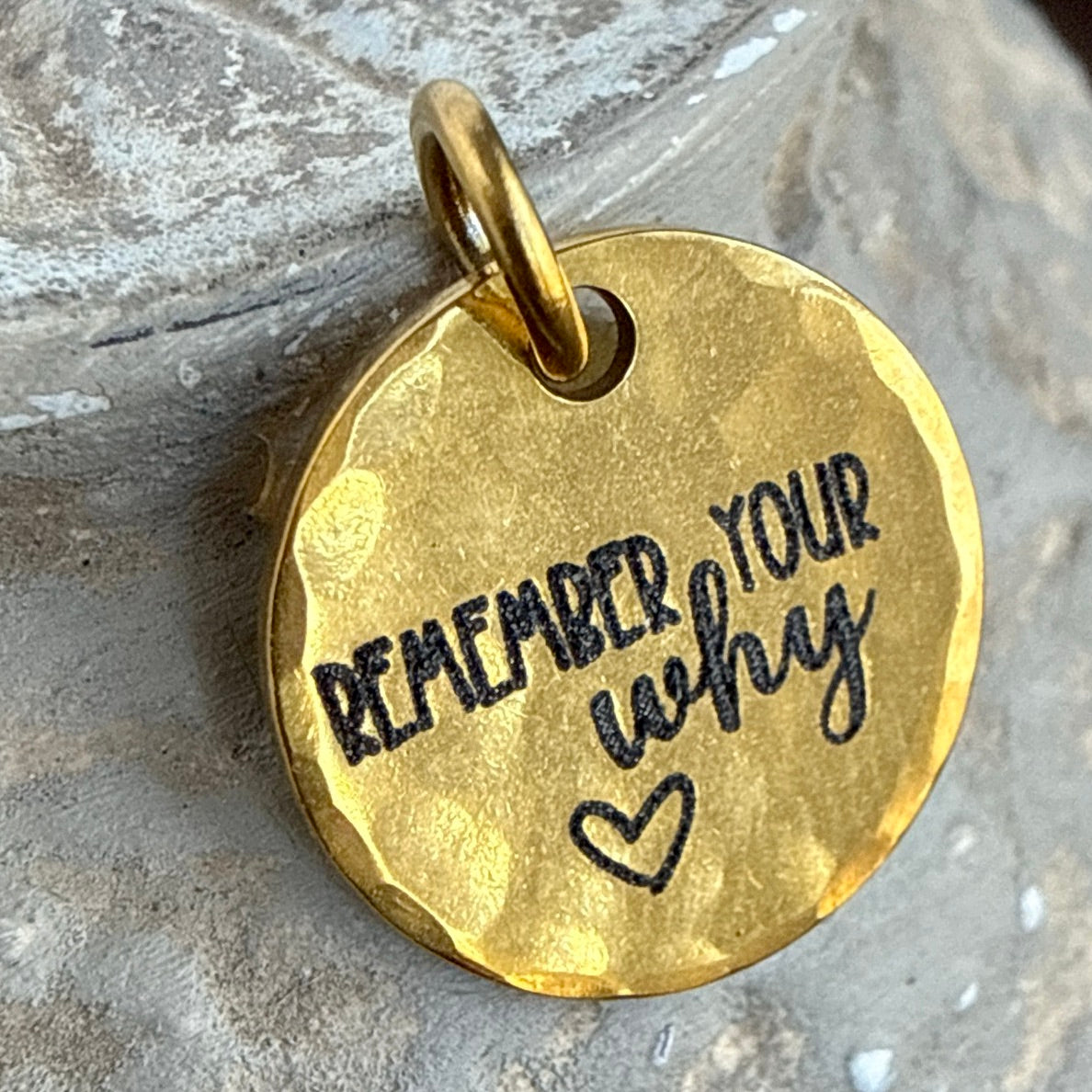 Gold pendant with 'Remember Your Why' engraving on a stone surface