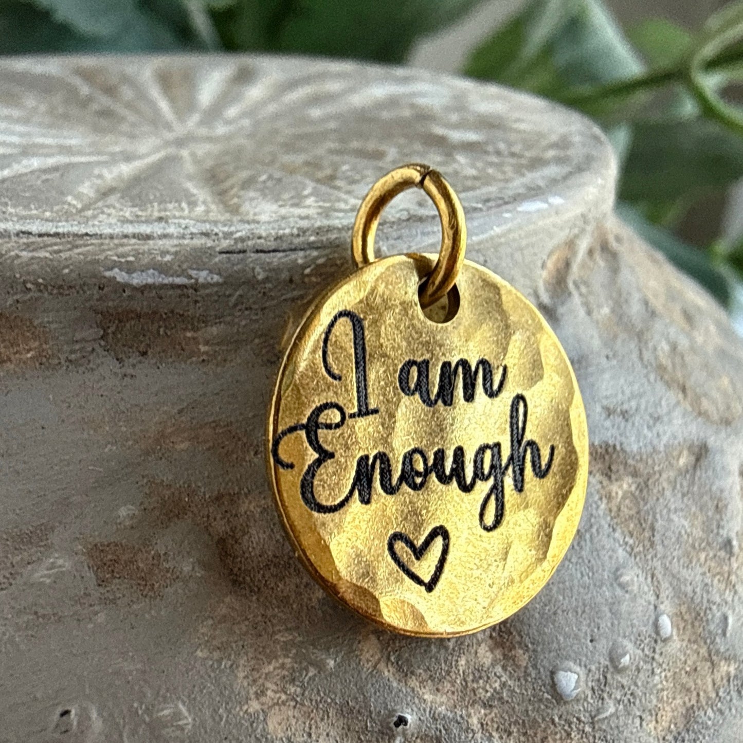 Gold pendant with 'I am Enough' engraving on a stone surface