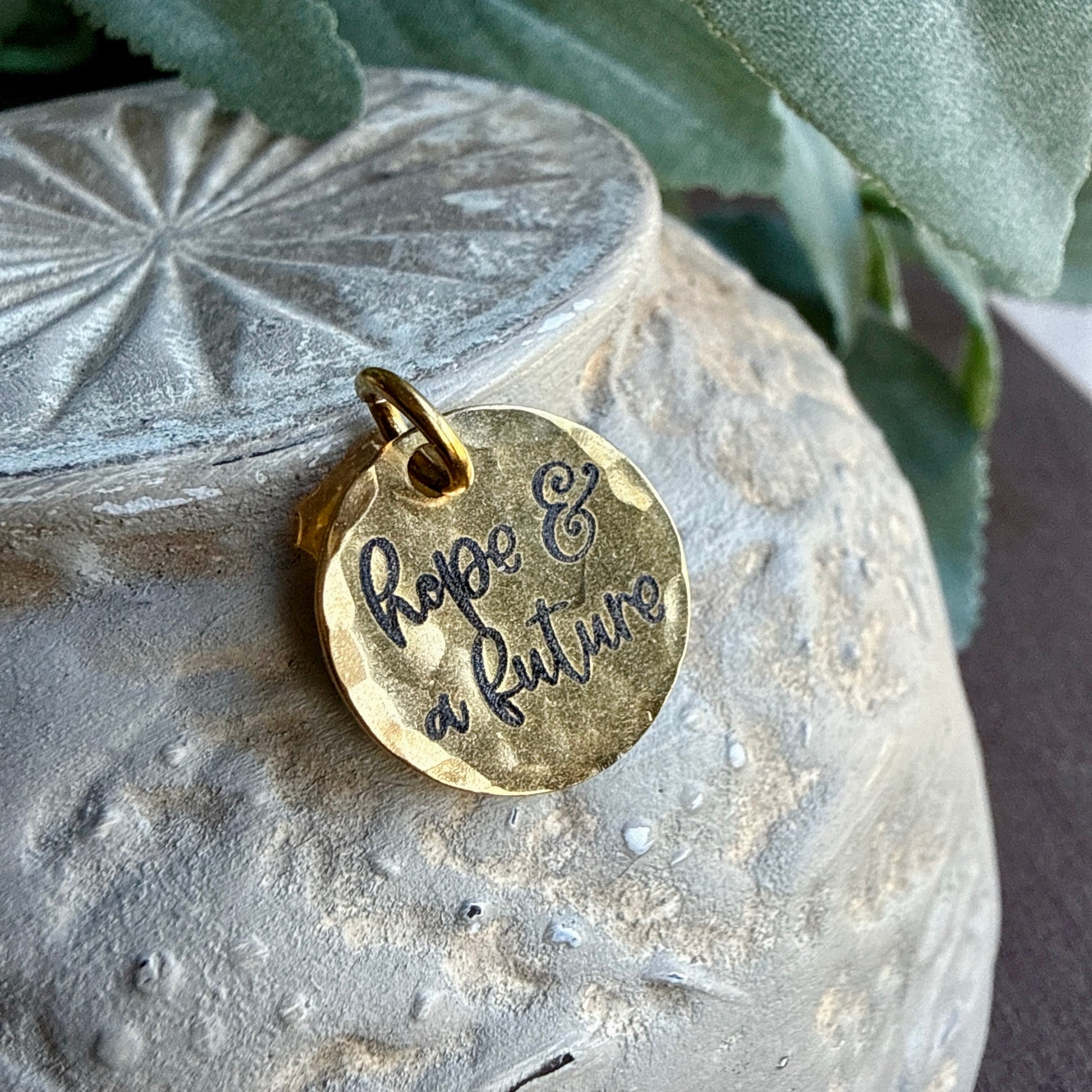 Gold pendant with 'hope & a future' engraving on a textured stone surface