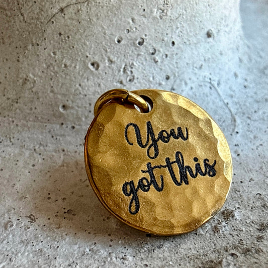 Gold pendant with 'You got this' engraving on a textured surface