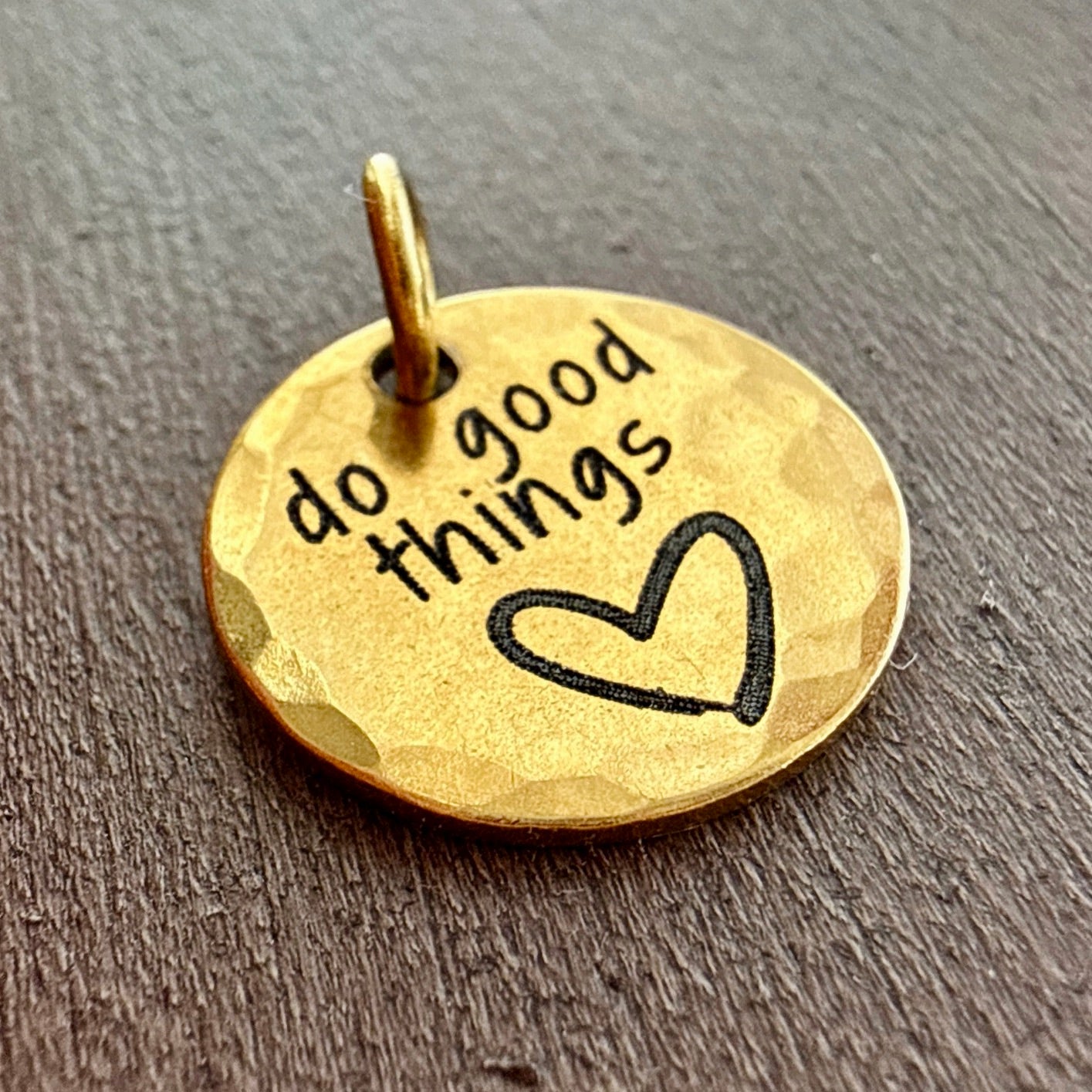 Gold pendant with 'do good things' engraving on a wooden surface